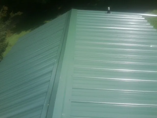 New green metal panels meeting at the ridge of a roof — Flat Roof Repair work by our crew in Beacon Falls