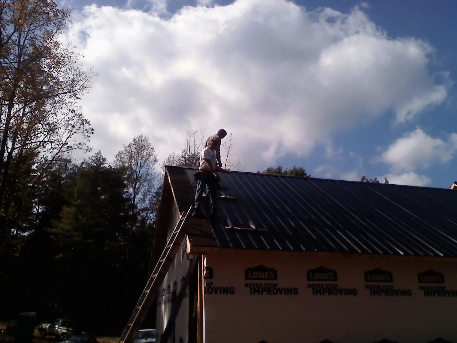 Roofer fastening dark metal panels high against a cloudy sky, from a Roof Inspection job in Beacon Falls